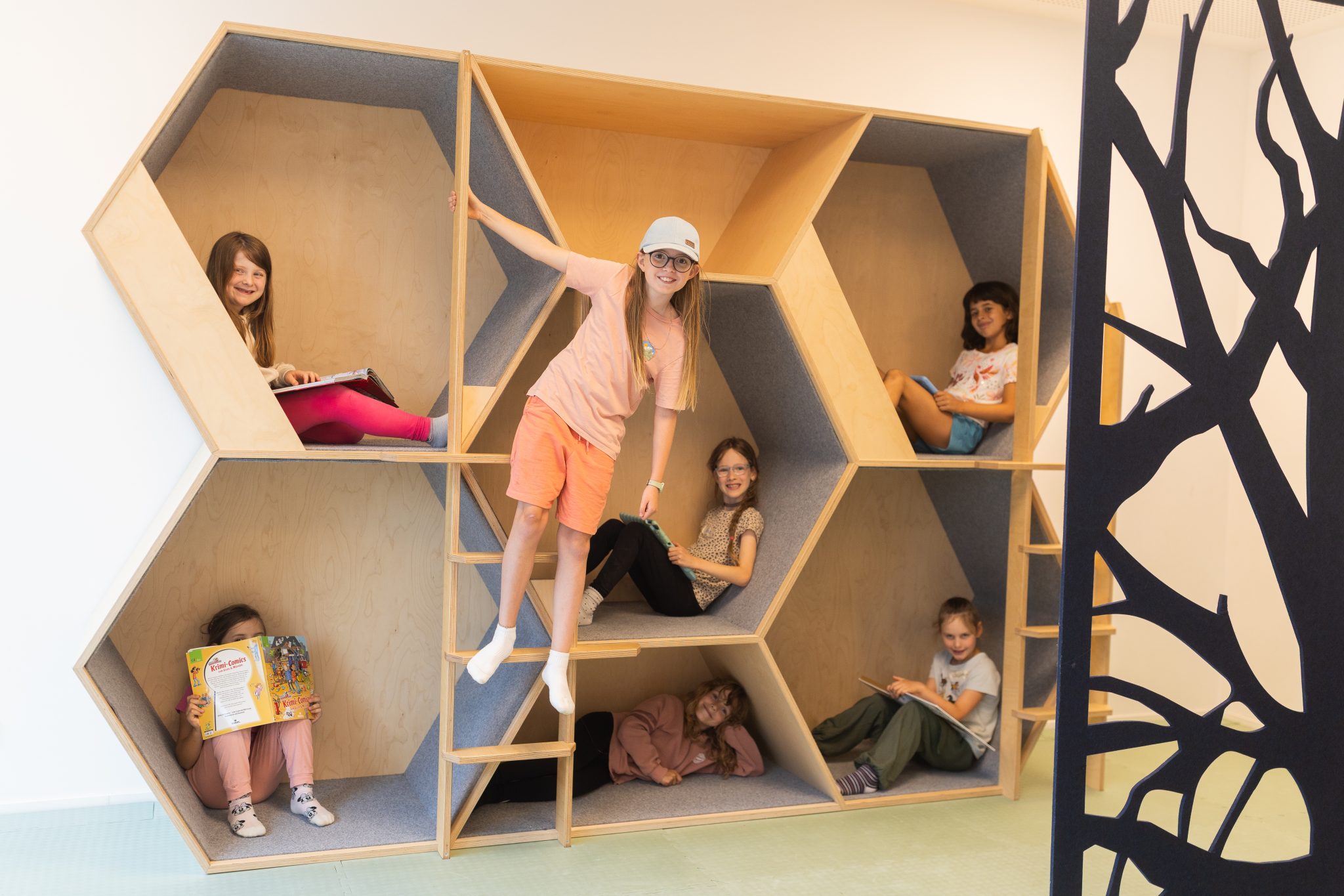 Kinder sitzen, lesen und spielen in einem mehrstöckigen, kindgerechten Rückzugs- und Spielmöbel in einer Kindertagesstätte in Ingolstadt.