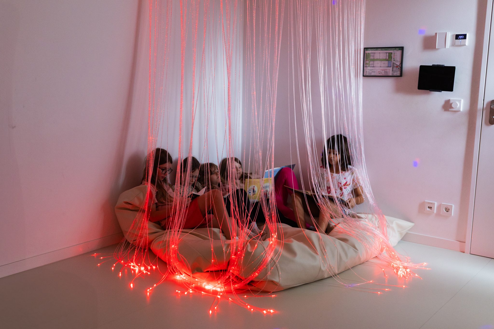 Kinder sitzen entspannt in einem Snoezelraum mit Lichtfasern und lesen gemeinsam in einer Kindertagesstätte in Ingolstadt.