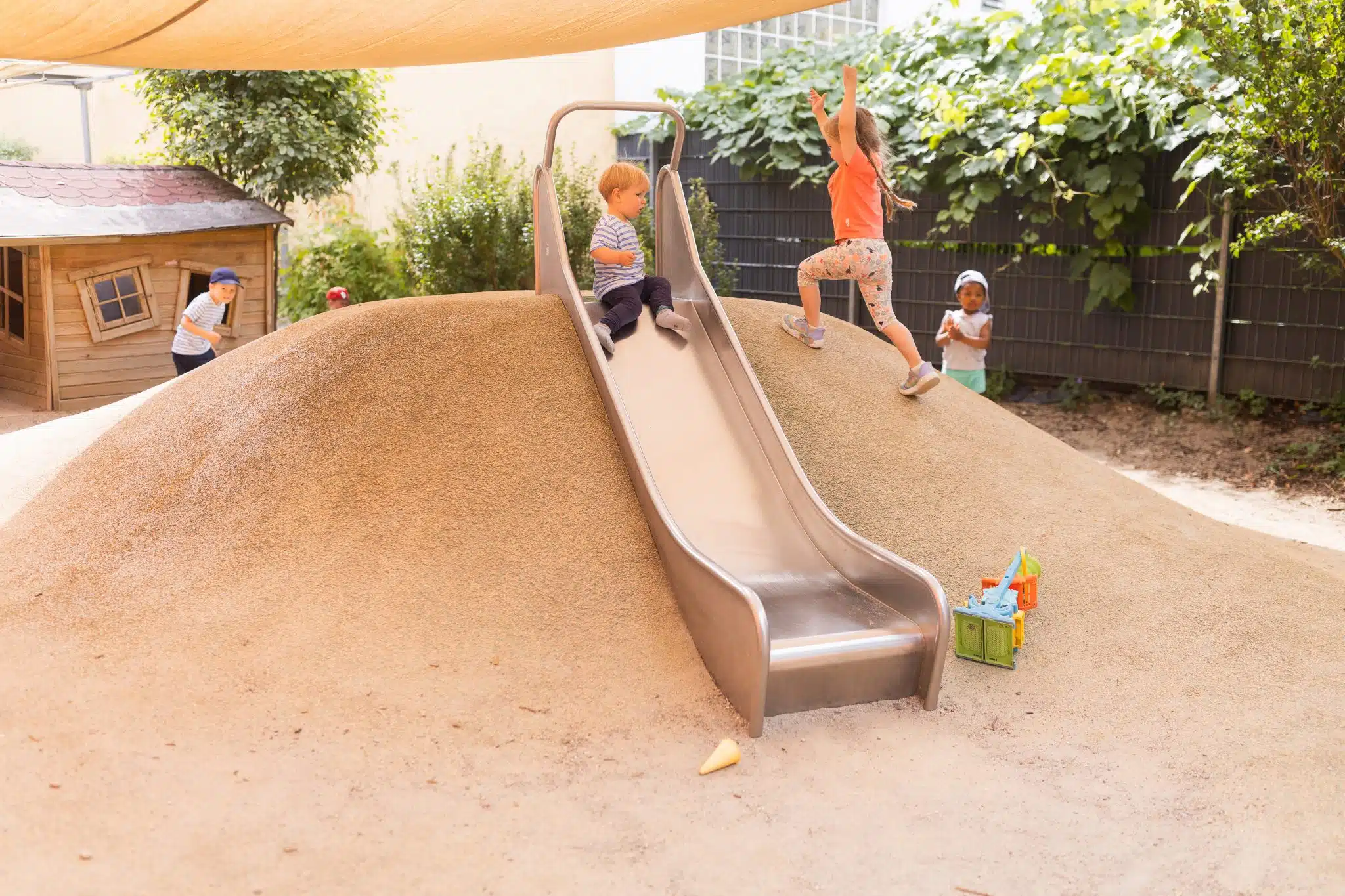 Kinder am Sandhügel mit Rutsche im Garten.