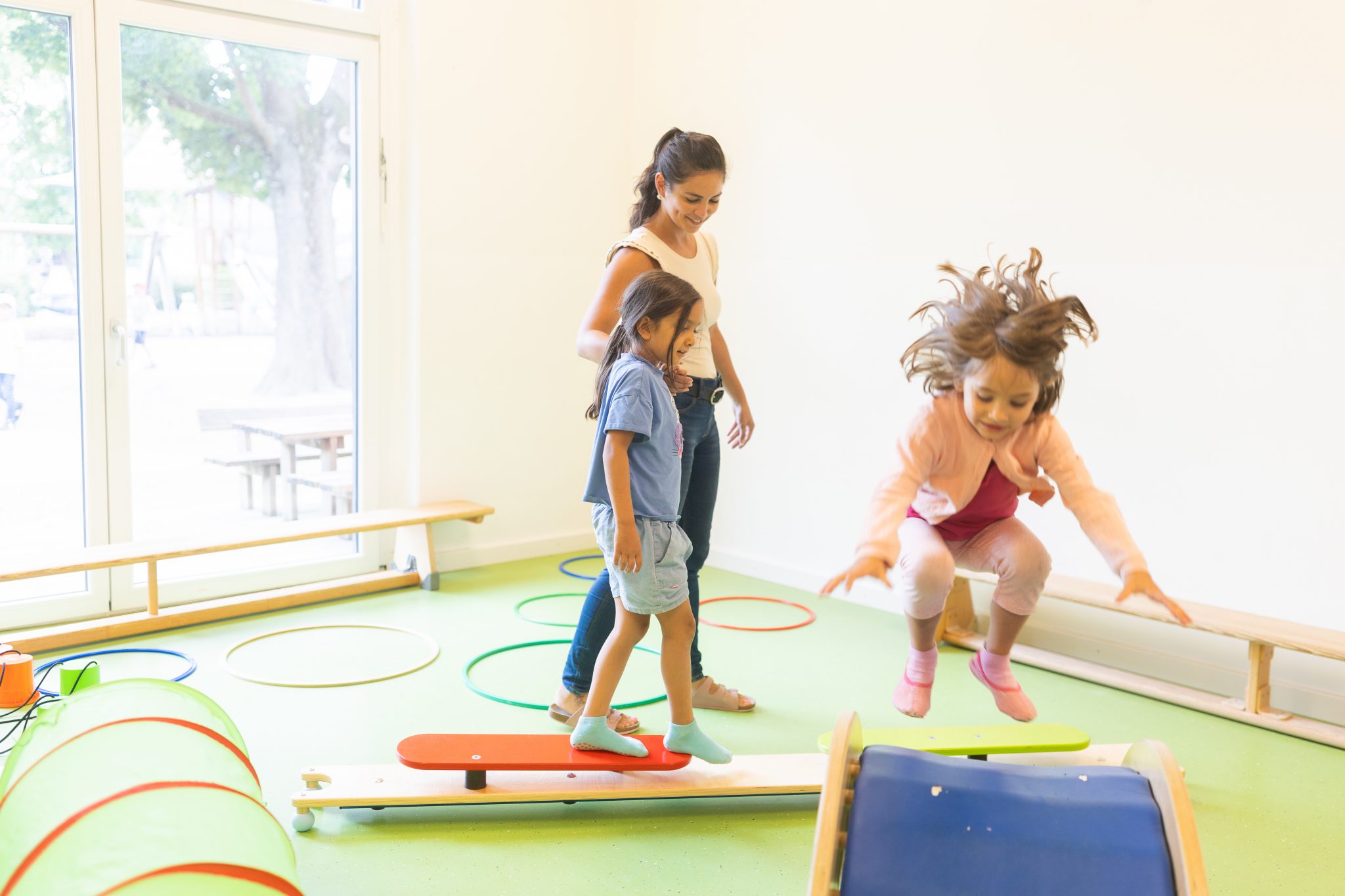 Kinder balancieren, springen und bewegen sich begleitet von einer Erzieherin in einem Bewegungsraum der bürgerhilfe ingolstadt KiTa GmbH