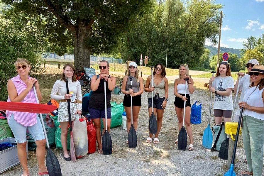 Team posiert mit Paddeln vor der Kanutour am Flussufer.