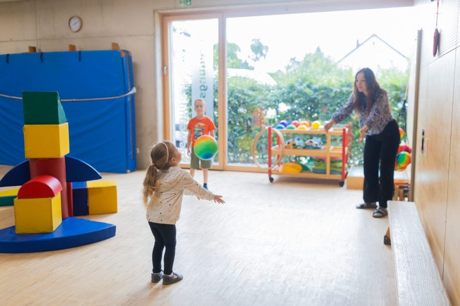 Kinder spielen mit bunten Bällen in einem Bewegungsraum gemeinsam mit einer Erzieherin in einer Kindertagesstätte der bürgerhilfe ingolstadt KiTa GmbH