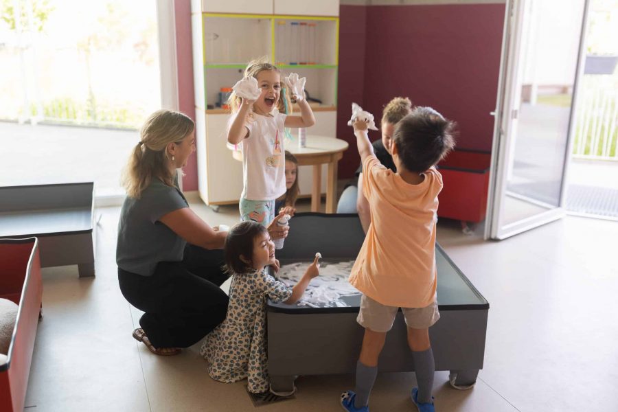 Kinder und Erzieherinnen am Spieltisch im Gruppenraum.