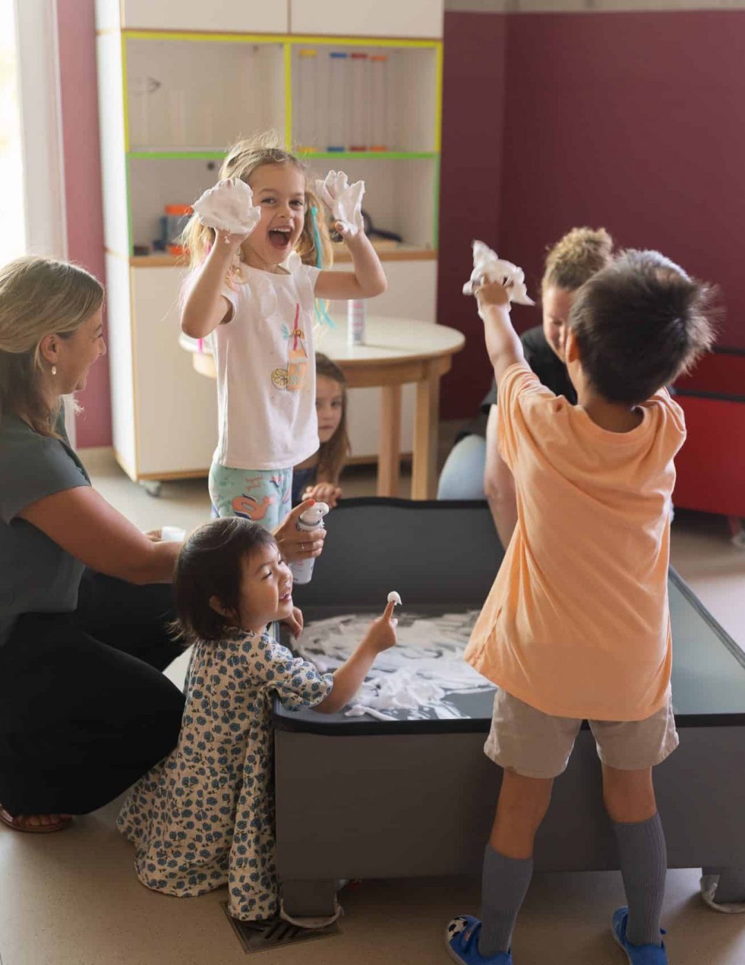 Kinder und Erzieherinnen am Spieltisch im Gruppenraum.