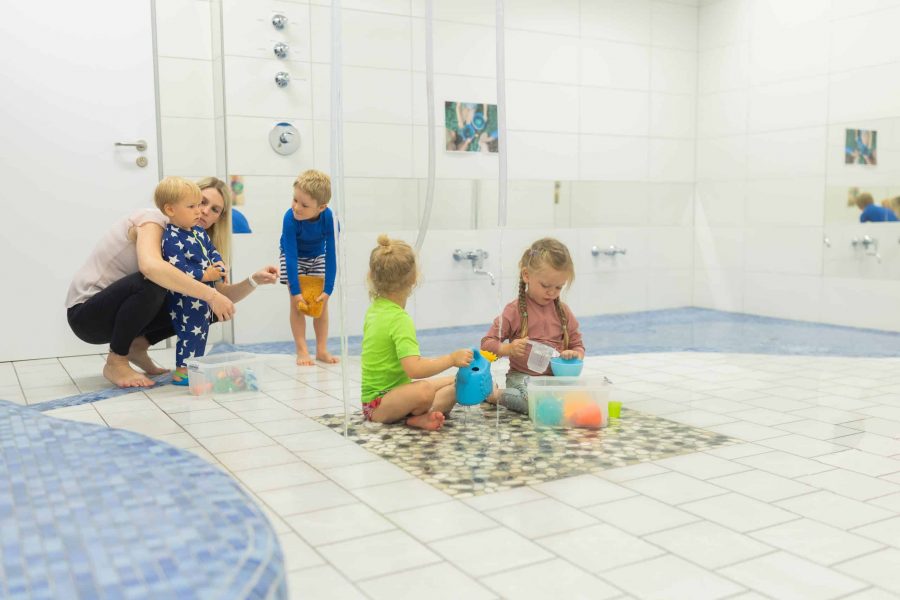 Kinder beim Wasserspiel am Boden mit Fachkraft.