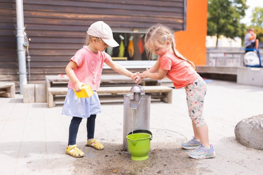 Zwei Kinder spielen an einer Wasserpumpe im Garten der Kita.
