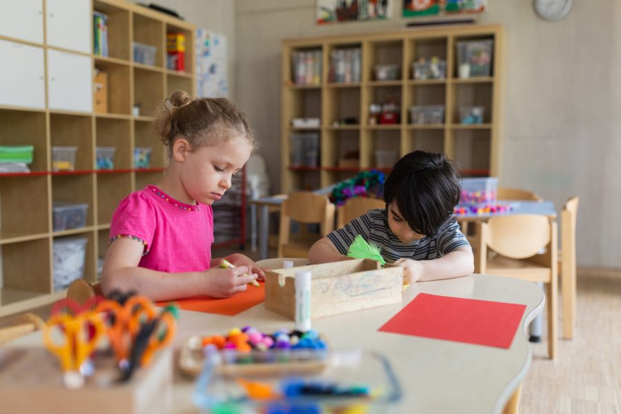 Zwei Kinder basteln konzentriert an einem Tisch im Gruppenraum einer Kindertagesstätte der bürgerhilfe ingolstadt KiTa GmbH