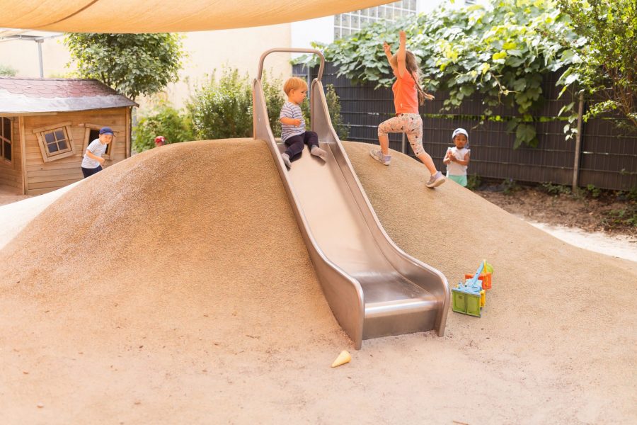 Kinder am Sandhügel mit Rutsche im Garten.