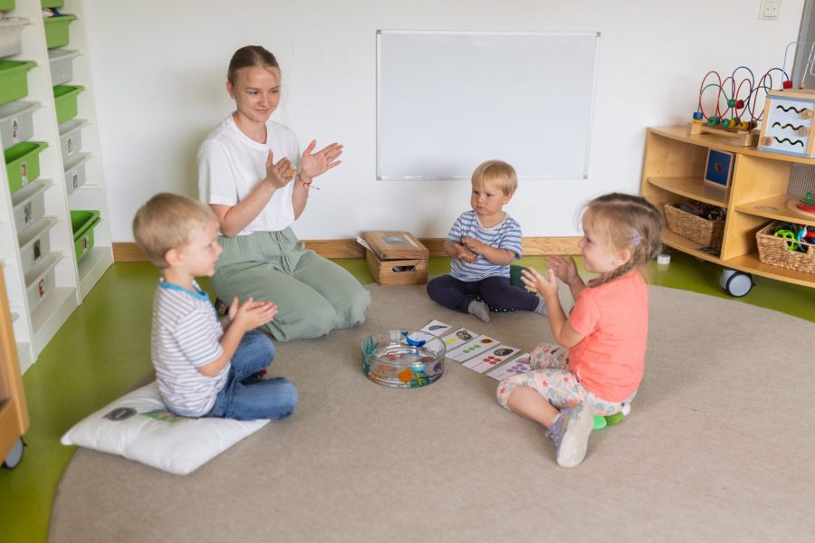 Erzieherin und Kleinkinder sitzen im Kreis und klatschen gemeinsam bei einer musikalischen Aktivität in einer Kindertagesstätte der bürgerhilfe ingolstadt KiTa GmbH