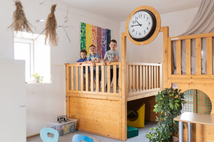 Kinder stehen auf einer hölzernen Galerie mit Uhr im Innenraum der bürgerhilfe ingolstadt KiTa GmbH