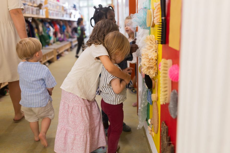 Mehrere Kinder stehen vor einer Wand mit verschiedenen Materialien und berühren diese gemeinsam.