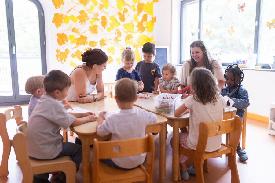 Mehrere Kinder und zwei Erwachsene sitzen an einem Tisch und gestalten gemeinsam mit Bastelmaterialien.
