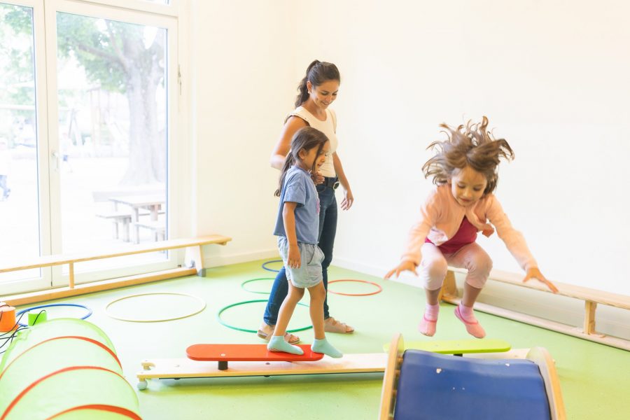 Kinder balancieren, springen und bewegen sich begleitet von einer Erzieherin in einem Bewegungsraum der bürgerhilfe ingolstadt KiTa GmbH