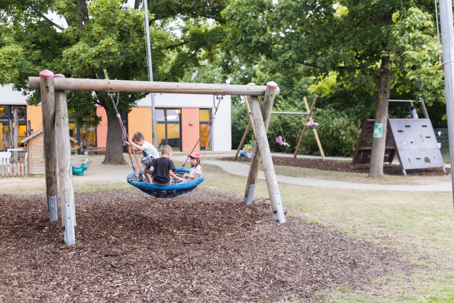 Kinder schaukeln gemeinsam auf einer Nestschaukel im Außengelände einer Kindertagesstätte der bürgerhilfe ingolstadt KiTa GmbH