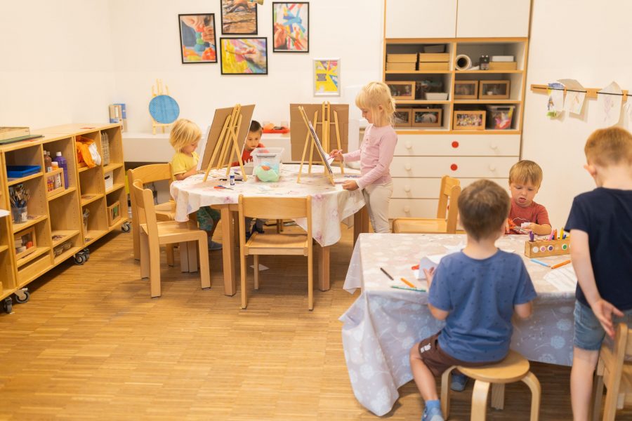 Kinder unterschiedlichen Alters malen und basteln gemeinsam an Tischen im Atelier einer Kindertagesstätte in Ingolstadt.