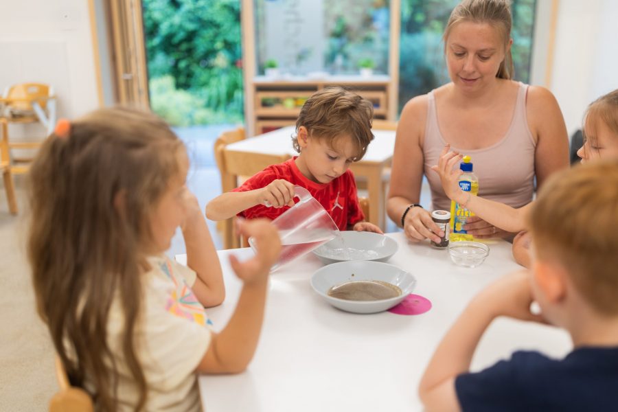 Kinder experimentieren gemeinsam mit Wasser und Materialien an einem Tisch in einer Kindertagesstätte in Ingolstadt, begleitet von einer Erzieherin.