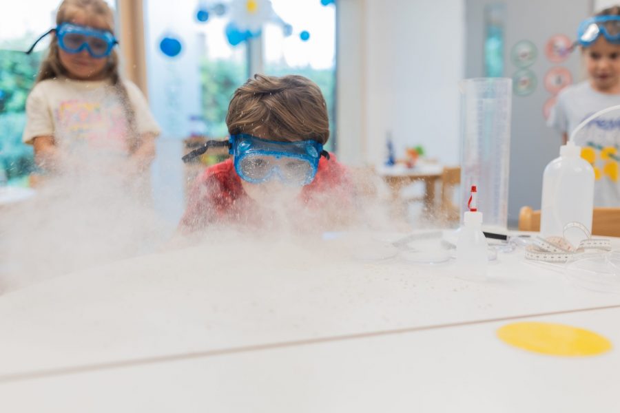 Ein Kind mit Schutzbrille beobachtet neugierig ein Experiment mit Dampf an einem Tisch in einer Kindertagesstätte in Ingolstadt.