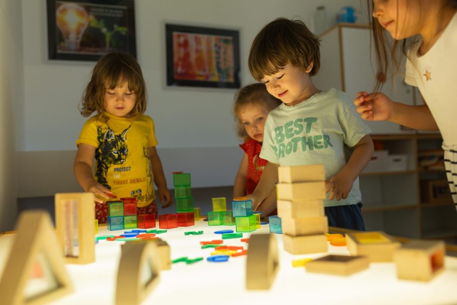 Kinder unterschiedlichen Alters spielen und bauen gemeinsam mit Bausteinen an einem Leuchttisch in einer Kindertagesstätte in Ingolstadt.