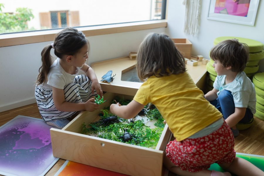 Kinder spielen gemeinsam mit Naturmaterialien in einer Spielkiste im Innenraum einer Kindertagesstätte in Ingolstadt.