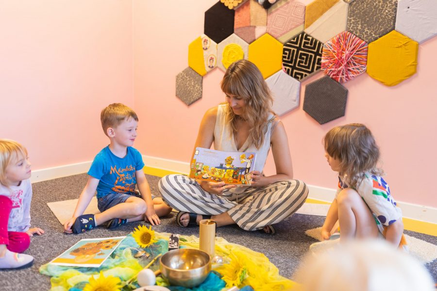 Eine pädagogische Fachkraft sitzt mit Kindern im Kreis und betrachtet gemeinsam ein Bilderbuch in einer Kindertagesstätte in Ingolstadt.