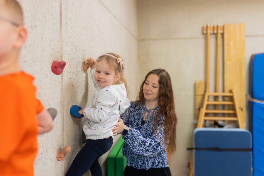 Erzieherin unterstützt ein Kind beim Klettern an einer Indoor-Kletterwand in einer Kindertagesstätte der bürgerhilfe ingolstadt KiTa GmbH