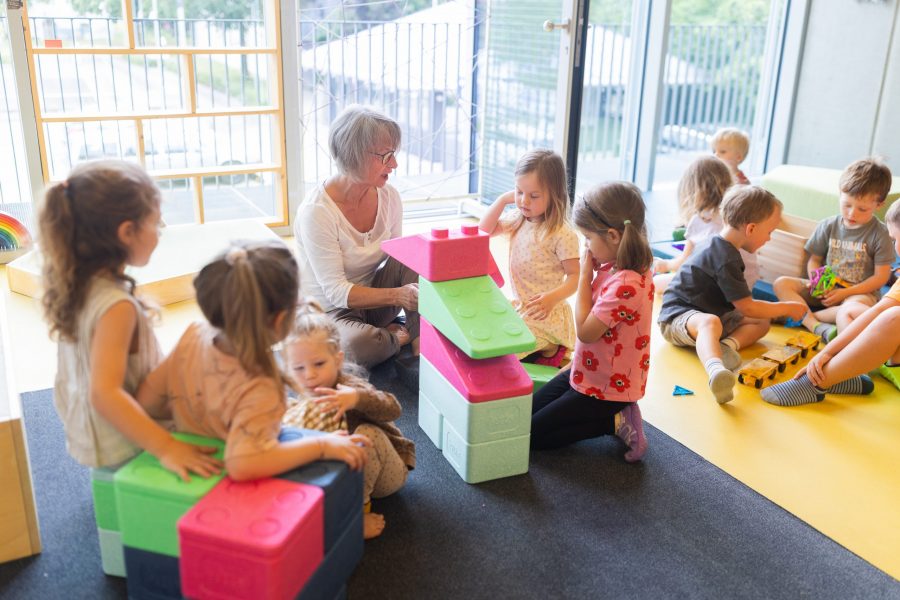 Kinder unterschiedlichen Alters spielen und bauen gemeinsam mit großen Bausteinen in einer Kindertagesstätte in Ingolstadt, begleitet von einer Erzieherin.