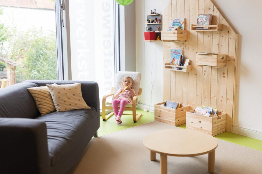 Ein Kind sitzt entspannt in einer gemütlichen Leseecke einer Kindertagesstätte in Ingolstadt.