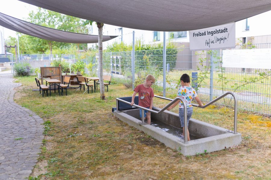 Kinder spielen barfuß an einer Wasseranlage im Außenbereich einer Kindertagesstätte der bürgerhilfe ingolstadt KiTa GmbH