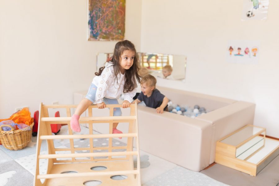 Ein Kind klettert auf einem Holzspielgerät im Innenraum einer Kindertagesstätte in Ingolstadt, andere Kinder spielen im Hintergrund.