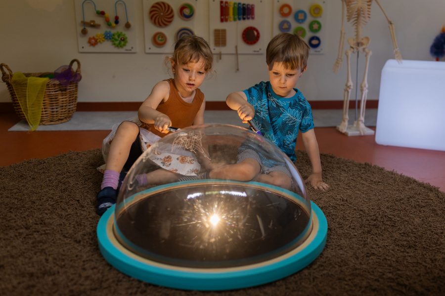 Zwei Kinder experimentieren gemeinsam mit einem Licht- und Spiegelelement im Innenraum einer Kindertagesstätte in Ingolstadt.