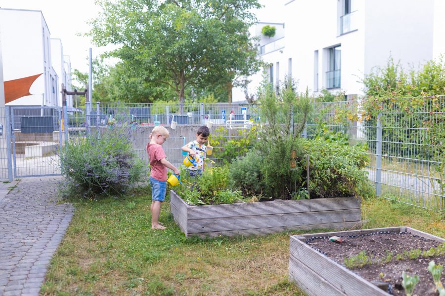 Kinder gießen Pflanzen am Hochbeet im Kita-Garten.