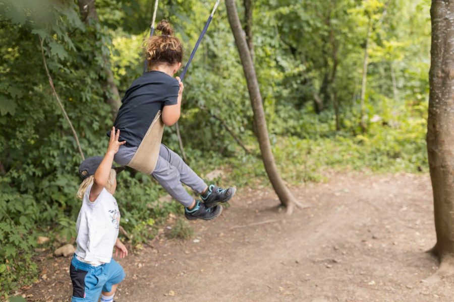 Zwei Kinder spielen mit einer Seilschaukel im Wald.