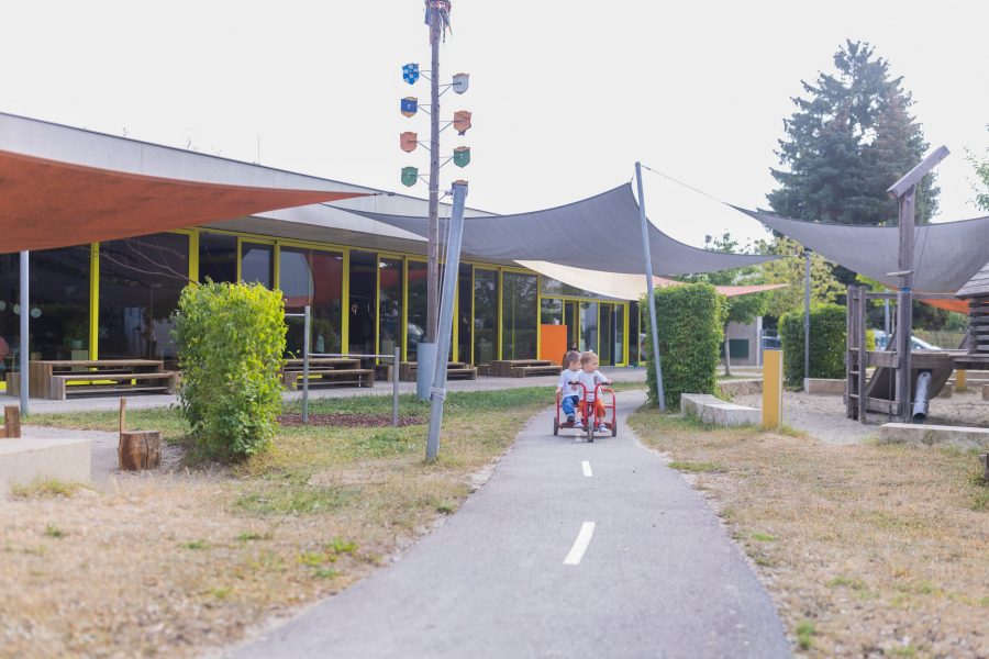 Kinder fahren gemeinsam mit einem Rutschauto auf dem Spielweg im Außengelände einer Kindertagesstätte der bürgerhilfe ingolstadt KiTa GmbH