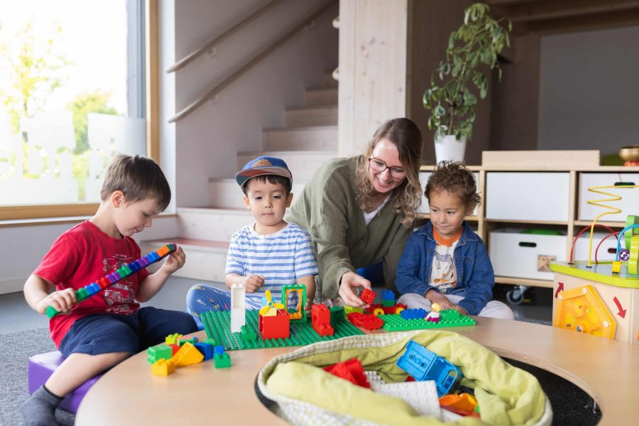 Erzieherin und Kinder bauen am Tisch.