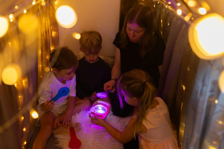 Vier Kinder und eine erwachsene Begleitperson sitzen in einer abgedunkelten Spielecke und betrachten leuchtende Objekte.