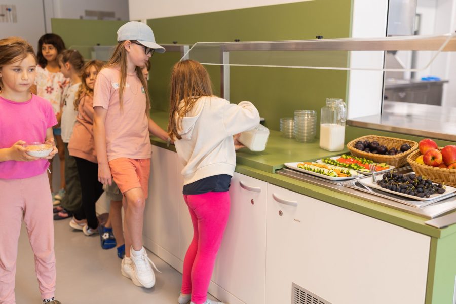 Kinder stehen am kindgerechten Essensbuffet einer Kindertagesstätte in Ingolstadt und bedienen sich selbstständig mit Lebensmitteln.