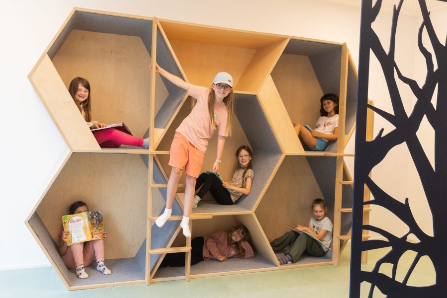 Kinder sitzen, lesen und spielen in einem mehrstöckigen, kindgerechten Rückzugs- und Spielmöbel in einer Kindertagesstätte in Ingolstadt.