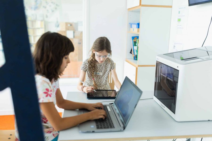 Kinder arbeiten mit Tablet und Laptop am Tisch der Kita.