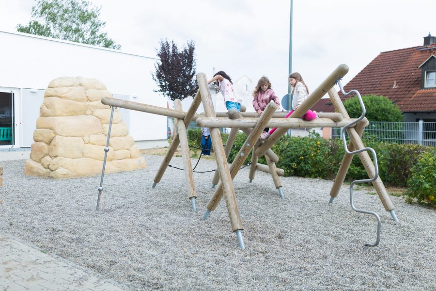 Kinder klettern und balancieren auf einem Holz-Kletterspielgerät im Außengelände einer Kindertagesstätte in Ingolstadt.