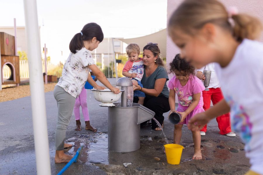 Kinder und Erzieherin an der Wasserstation im Garten.